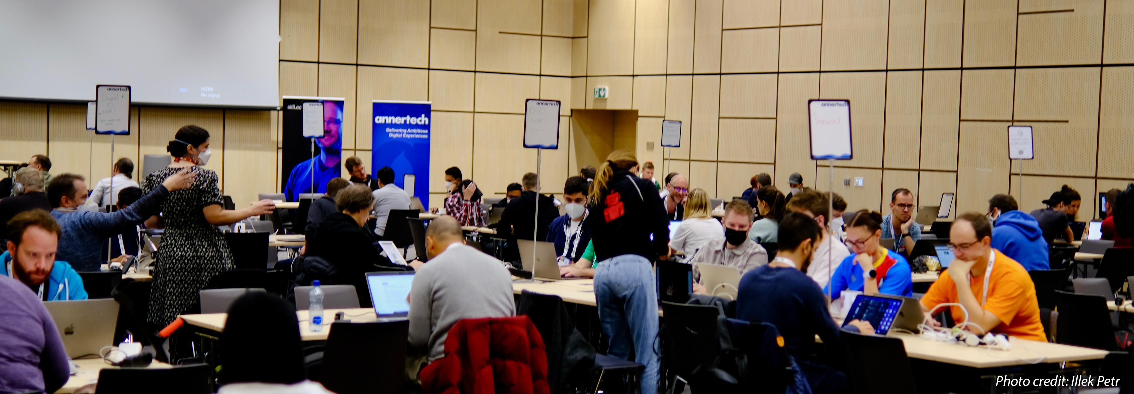 Contributors at DrupalCon Prague stand or sit with laptops and talk