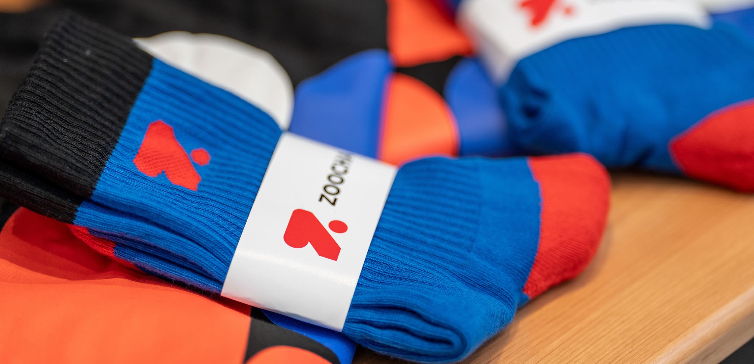 A pair of socks sitting on a pile of shirts, with a 'Z' logo and the word 'Zoocha' on the wrapping paper.