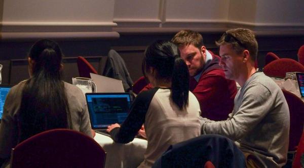 larowlan sits at a table using his laptop while another contributor looks on