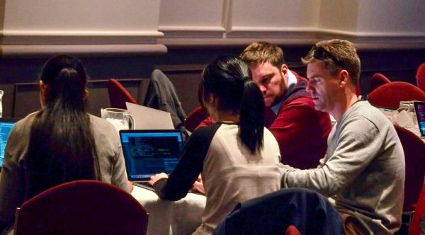 larowlan sits at a table using his laptop while another contributor looks on.
